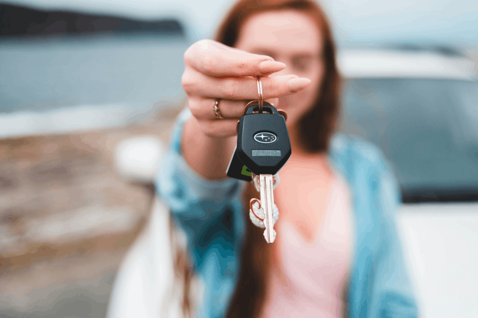 Person confidently holding car keys, smiling beside their new car